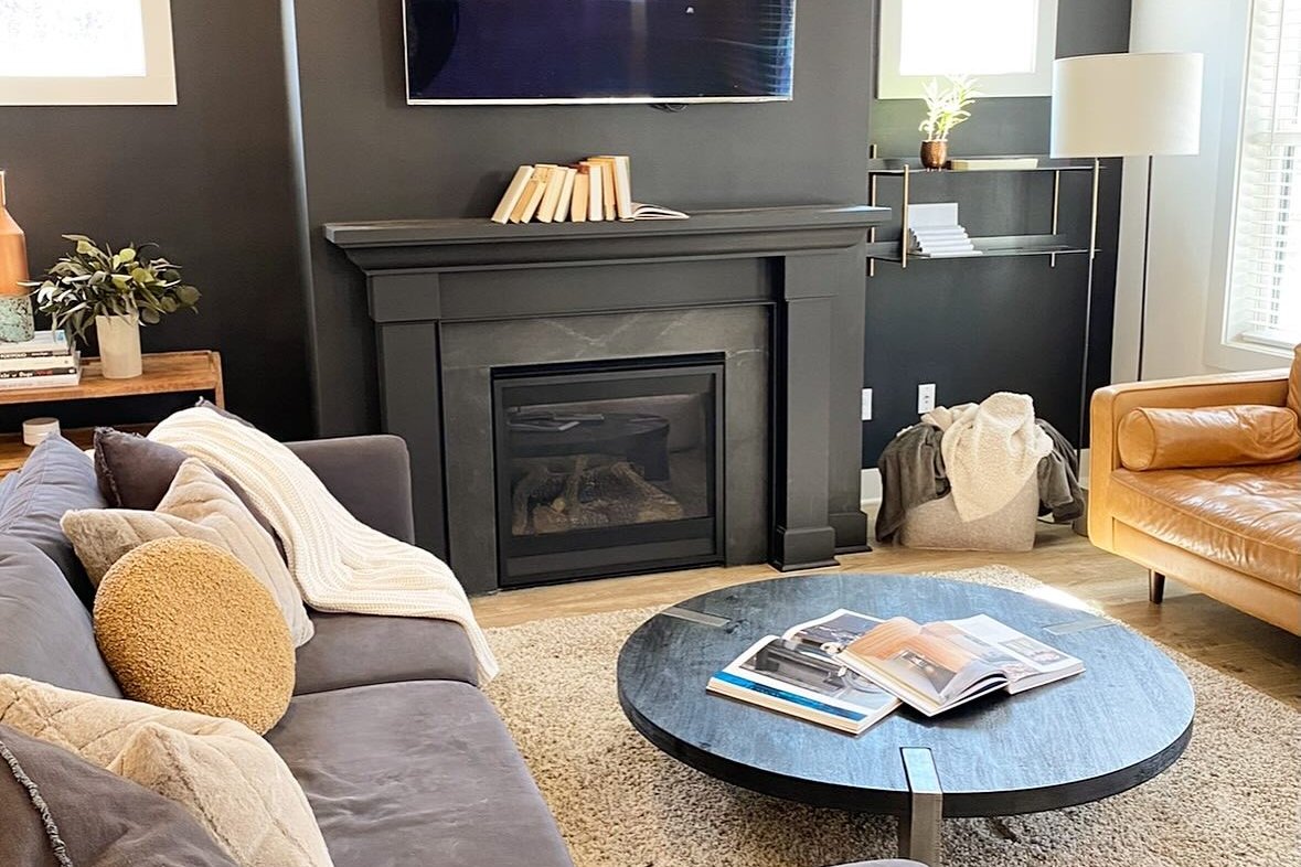 A cozy living room with a charcoal fireplace wall, gray sectional and round coffee table