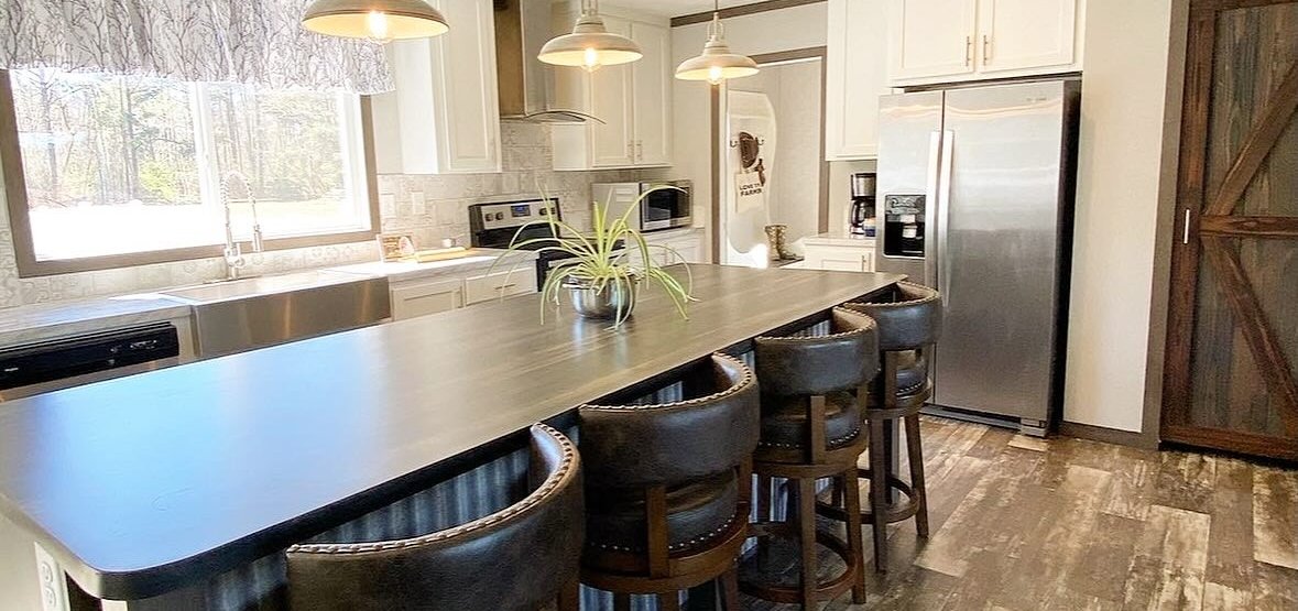 A kitchen with a long island, wood-look floors and leather bar stools, staged for sale
