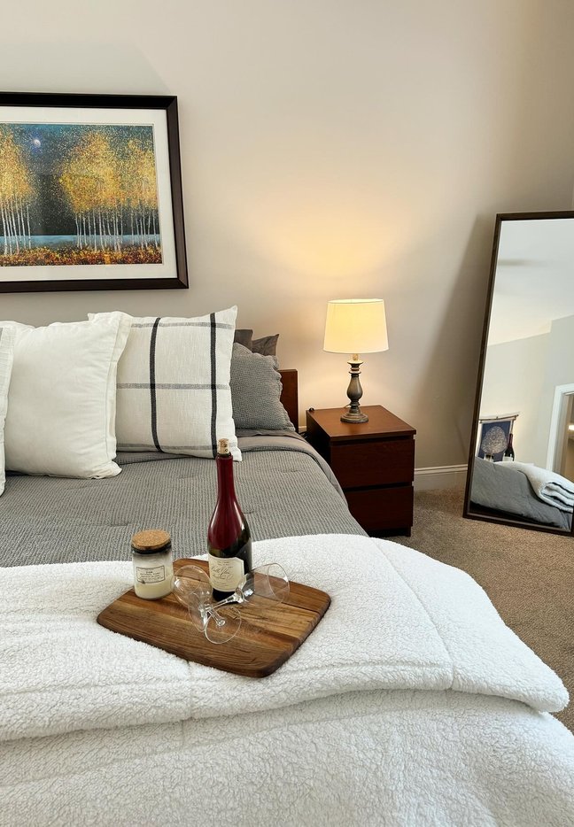 A staged bed with a wine tray, mirror and layered bedding